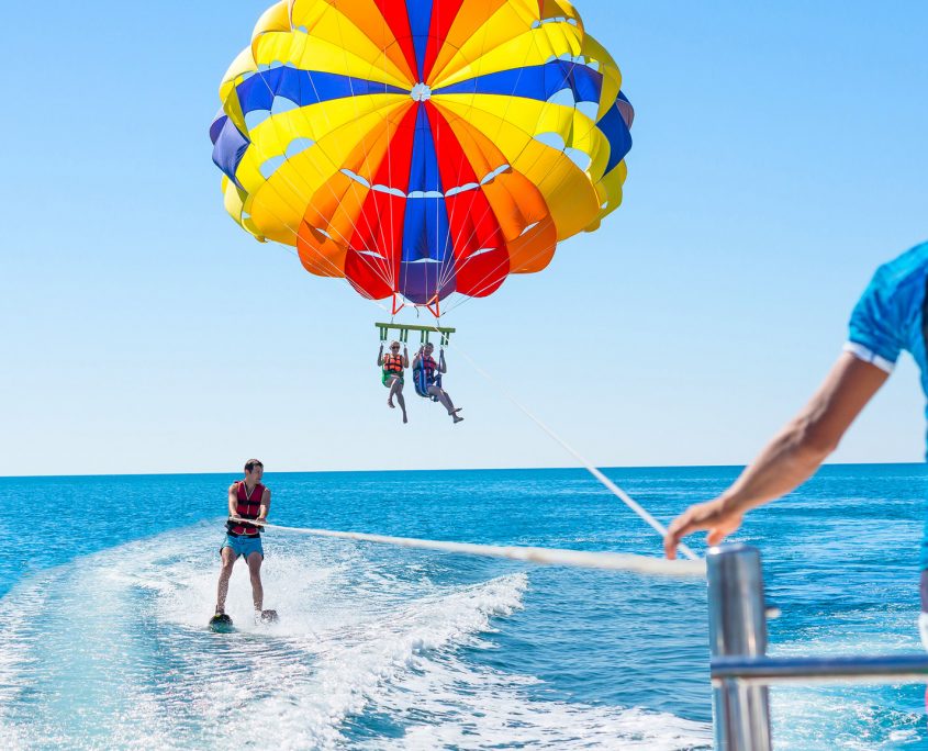 Asaya-Hills-Villas-Parga-Greece-sea-parasailing-waterskiing-watersports-holidays Two people parasailing and one person waterskiing in the sea in front of an instructor on a sunny day.