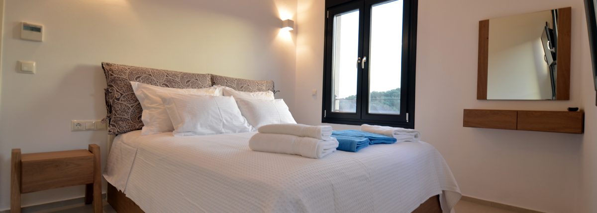Asaya-Hills-Villas-Parga-Greece-private-villas-bedroom-double-bed-window-with-view-mirror A bedroom with a double bed, a side window, shower towels and a mirror of a private villa at Asaya Hills Villas, Parga, Greece.