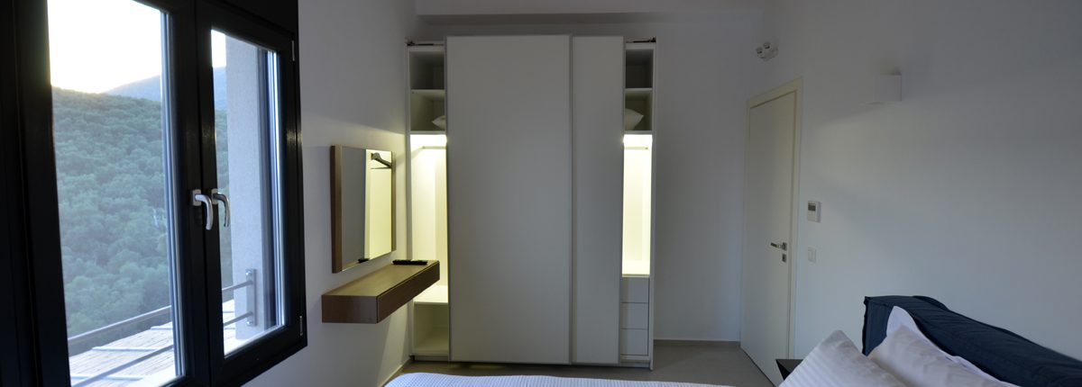 Asaya-Hills-Villas-Parga-Greece-private-villas-bedroom-double-bed-closet-window-with-a-view Bedroom with a double bed looking at a window with a view, a white closet and a wooden ceiling of a private villa at Asaya Hills Villas, Parga, Greece.