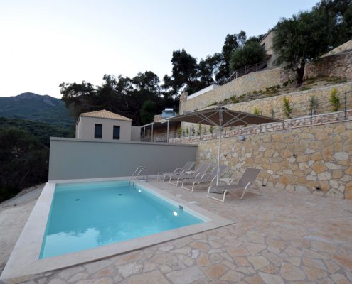 Asaya-Hills-Villas-Parga-Greece-private-villas-swimming-pool-sunbeds-umbrella-view A swimming pool with four sunbeds and an umbrella at the exterior space of a private villa at Asaya Hills Villas, Parga, Greece.