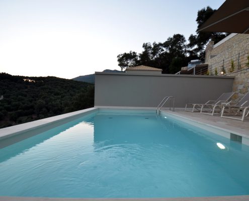 Asaya-Hills-Villas-Parga-Greece-private-villas-swimming-pool-sunbeds-view A swimming pool with sunbeds at the exterior space of a private villa overlooking a hill at Asaya Hills Villas, Parga, Greece.