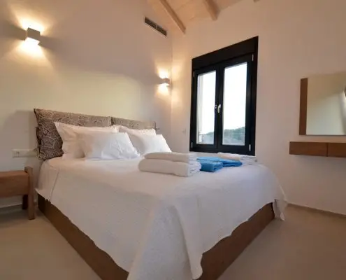 A bedroom with a double bed, a side window, shower towels and a mirror of a private villa at Parga, Greece.