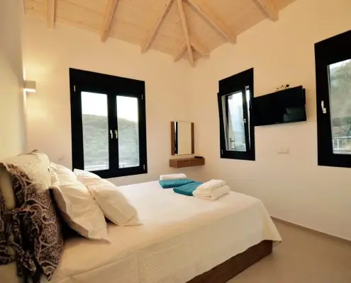 A three window bedroom with a double bed, shower towels, TV and a wooden ceiling of a private villa at Parga, Greece. 