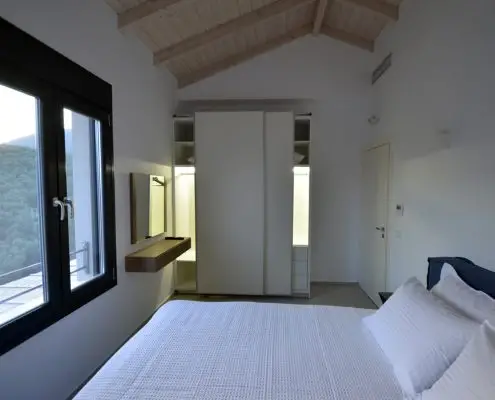 Bedroom with a king-size bed looking at a window with a view, a white closet and a wooden ceiling of a private villa at Parga, Greece.