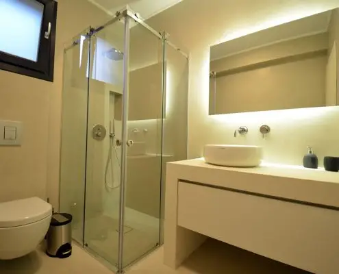 A modern minimal bathroom with a glass door shower and a large mirror of a private villa at Parga, Greece. 