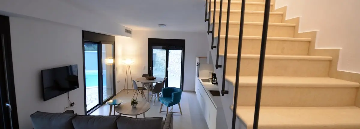 Living room and kitchen with modern furniture and a staircase leading to the upper floor of a private villa at Parga, Greece.
