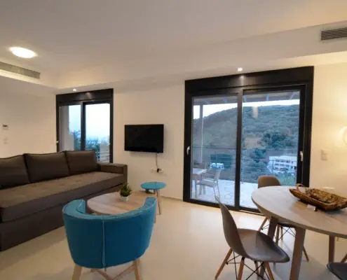 Living room with a sofa, coffee table, dinner table and large balcony doors leading to the balcony at the base floor of a private villa at Parga, Greece.