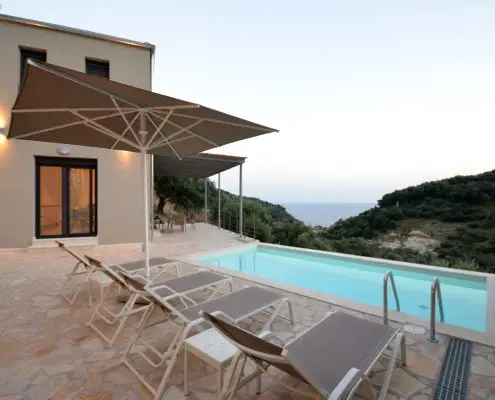 Exterior space of a private villa with a swimming pool, sunbeds, umbrella and balcony overlooking at the sea at Parga, Greece. 