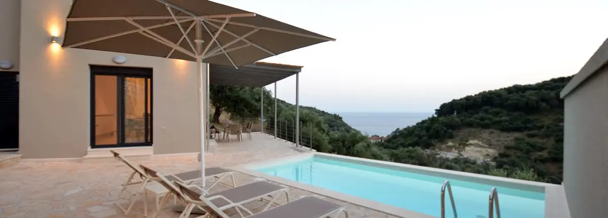 Exterior space of a private villa with a swimming pool, sunbeds, umbrella and balcony overlooking at the sea at Parga, Greece. 