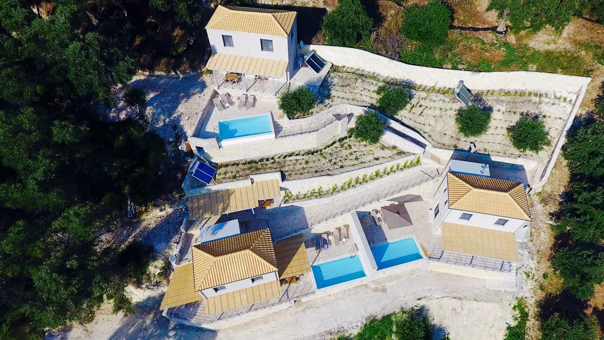 Aerial shot of three private villas with swimming pools surrounded by trees at Asaya Hills Villas, Parga, Greece.
