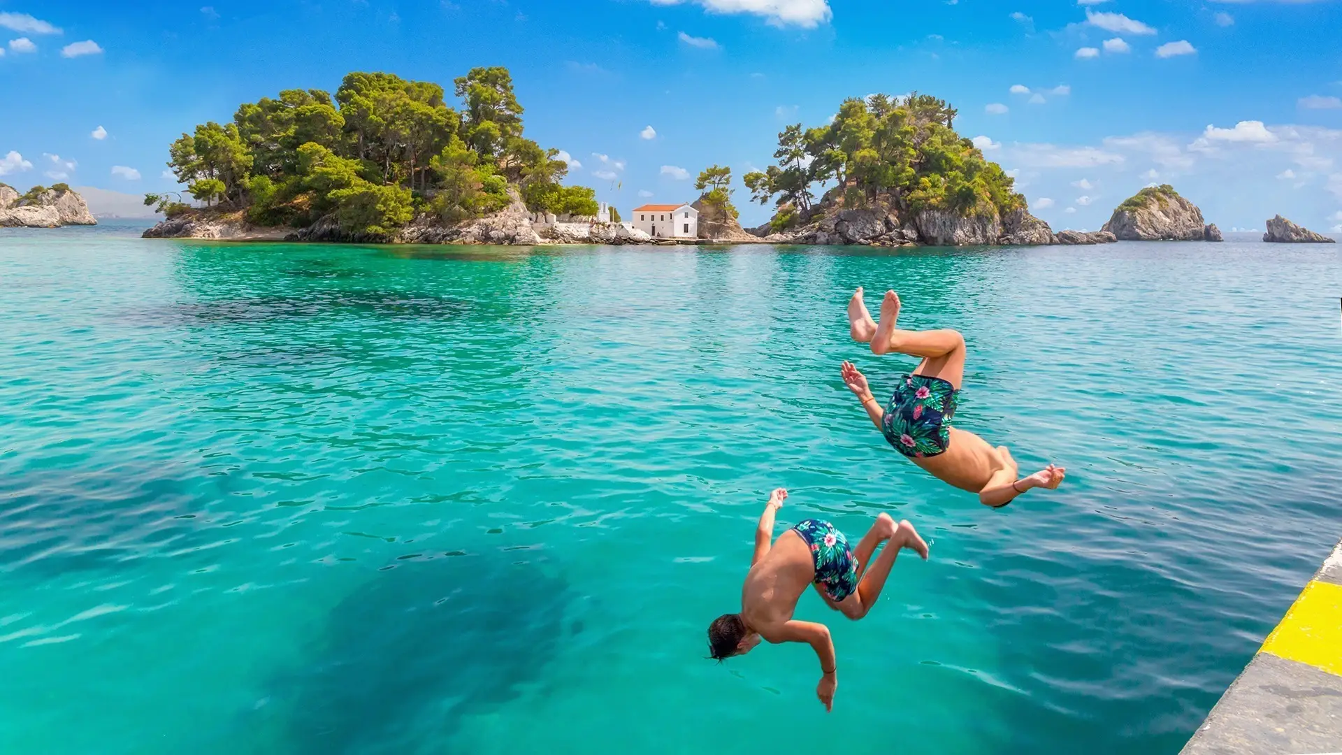 Two boys jumping into the sea on a sunny day at Parga port, Greece.