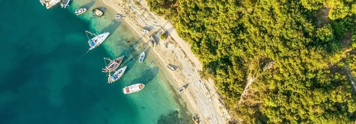 Asaya-Hills-Villas-Parga-Greece-beach-boats-nature-holidays Aerial view of a beach with crystal turquoise waters and boats near the shore at Parga, Greece.